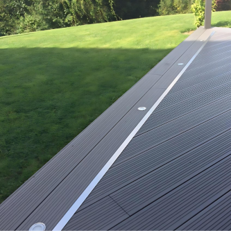 Terrasse en composite gris anthracite avec finition en aluminium, spots encastrés et pelouse verdoyante.