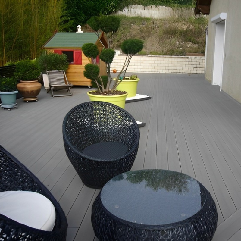 Terrasse moderne en composite gris anthracite, avec salon de jardin et pot de fleurs Fuji, alliant confort et esthétique.